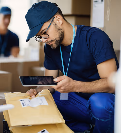 Delivery worker wearing a cap and glasses scanning a package with a handheld device.