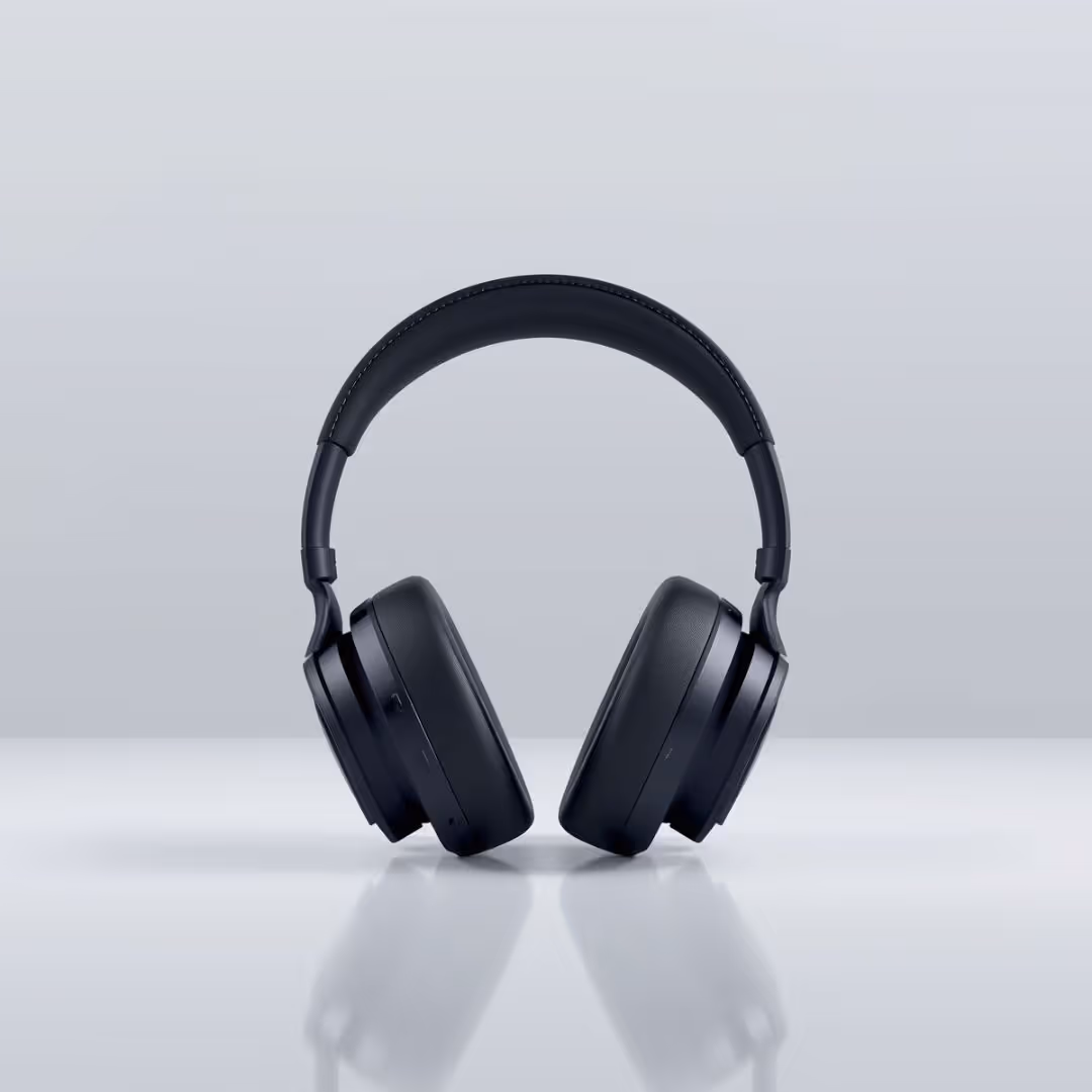Black over-ear headphones standing upright on a reflective surface with a light gray background.