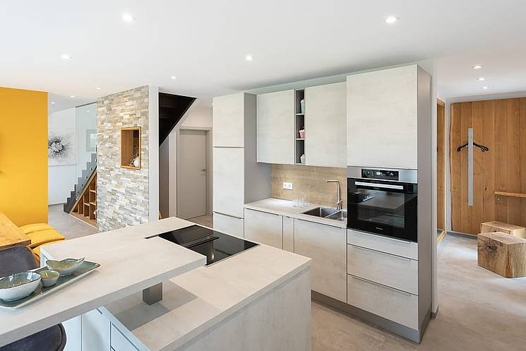 Einfamilienhaus mit Flachdach Innenansicht moderne offene Küche mit Kochinsel und Natursteinwand