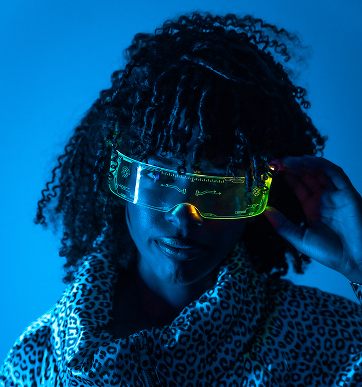 Person with curly hair wearing neon-lit futuristic visor and leopard-print jacket against a blue background.
