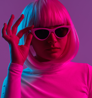 Person with a white bob haircut wearing pink cat-eye sunglasses and a long-sleeve shirt under magenta and blue lighting.
