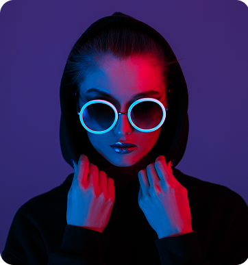 Person wearing round illuminated glasses and a black hoodie, lit with blue and red lighting against a dark background.