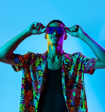 Young man wearing a colorful floral shirt and futuristic purple sunglasses against a bright blue background.