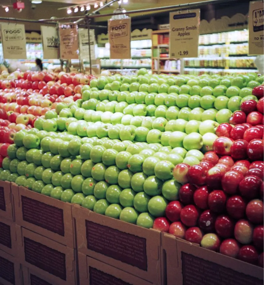 Rows of neatly stacked green and red apples displayed in a grocery store produce section.