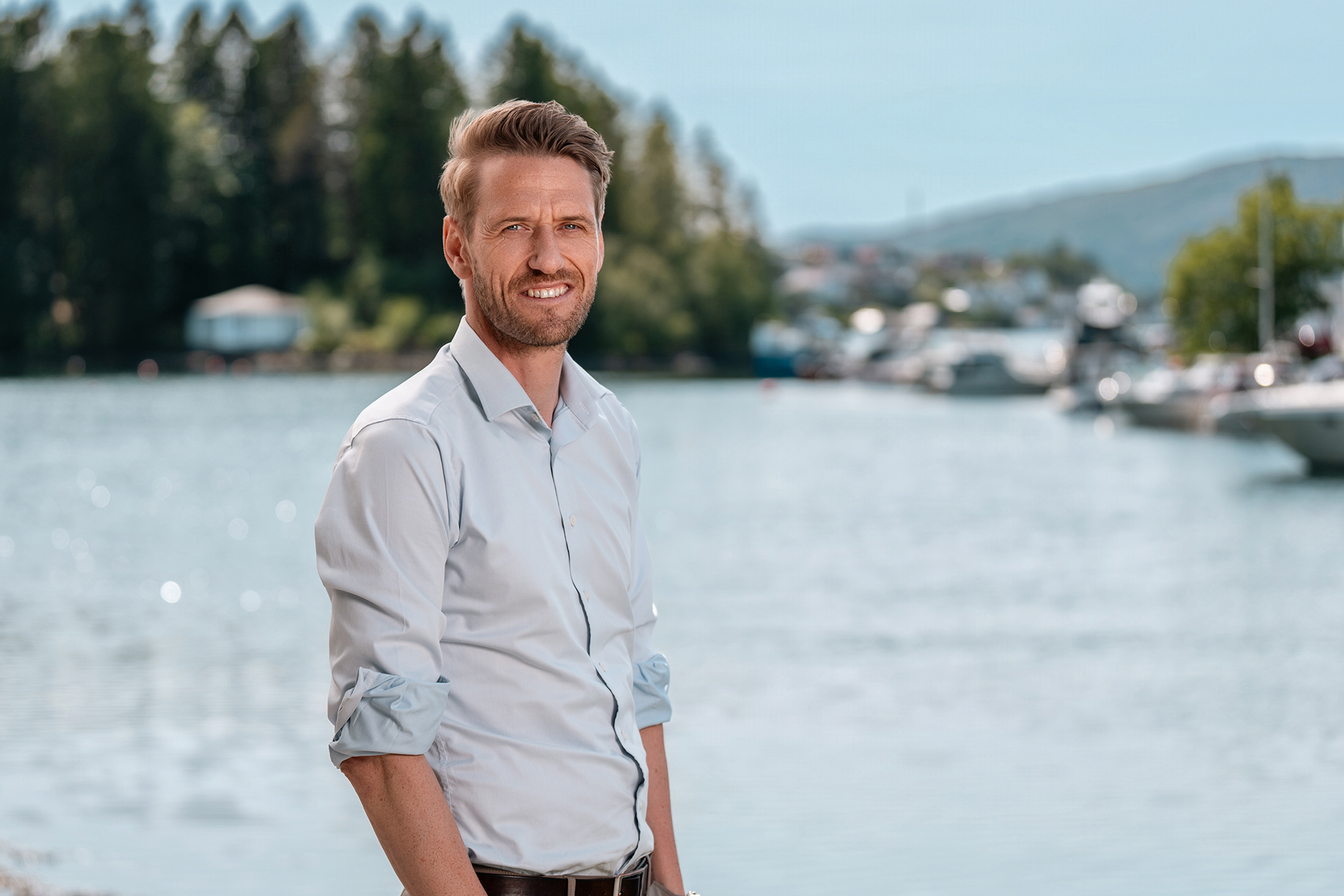 Bilde av Runar Brøste foran havet i Alvøen på en solrik dag med blå himmel. Båter og litt trær er synlig lengre bak på bildet.