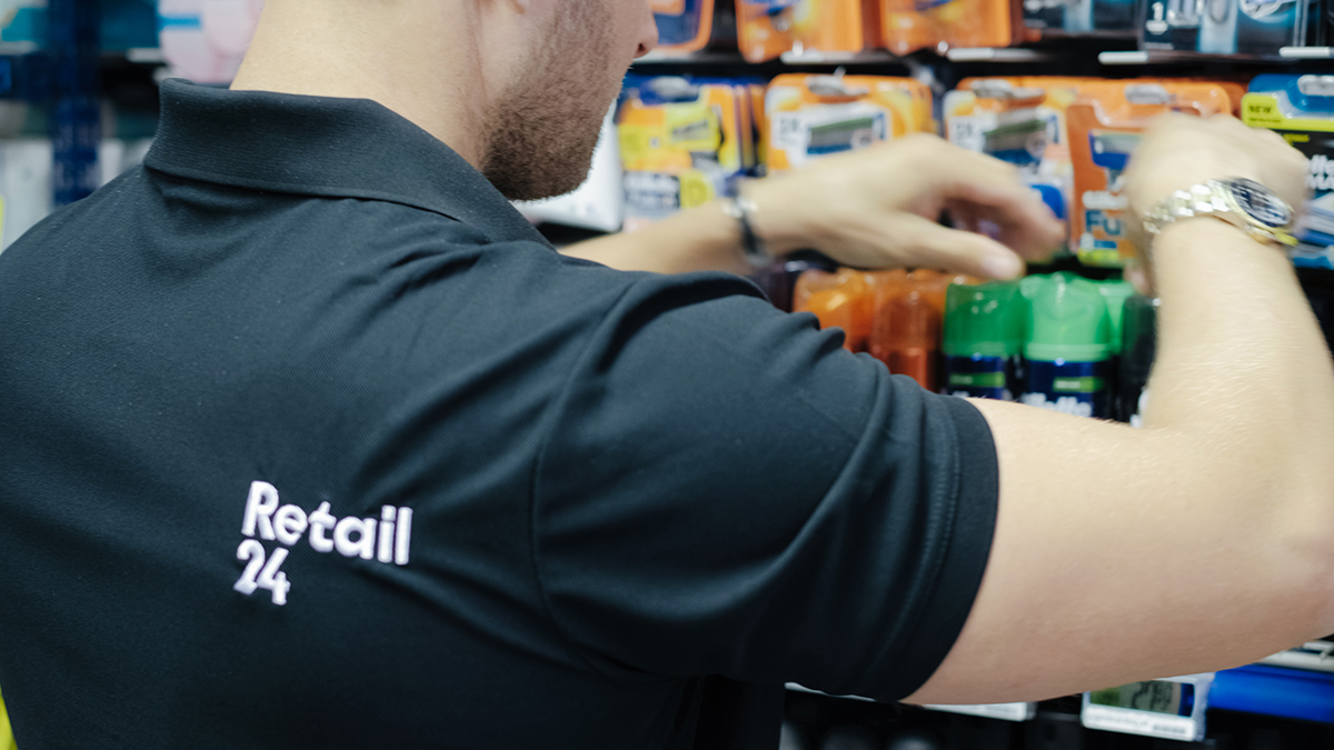 Person med logo Retail24 på ryggen rydder og steller i en butikkhylle