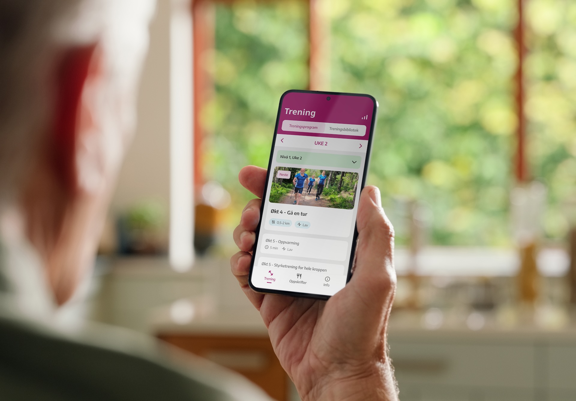 Eldre voksen holder en telefon med appen Hjertekampen foran seg selv.