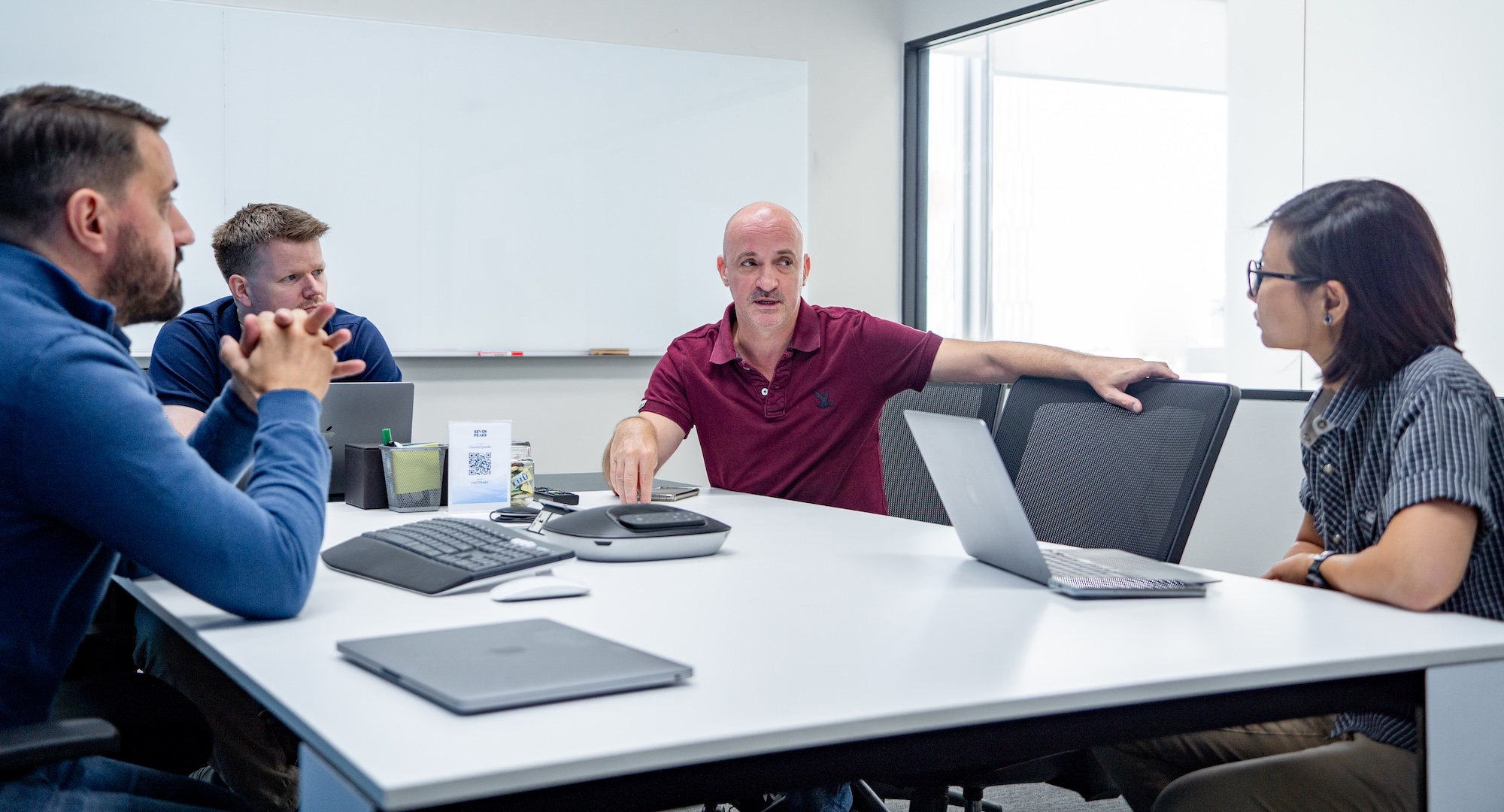 Fire personer som diskuterer rundt et hvit bord.