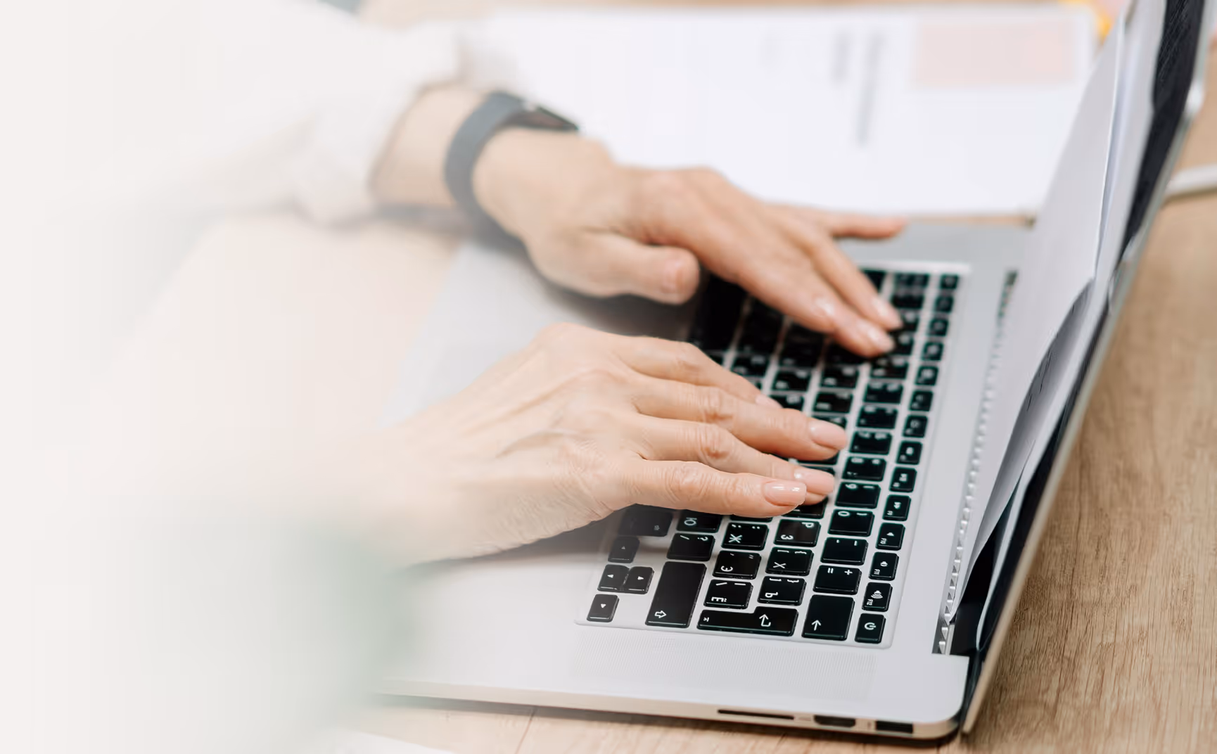 Person typing on a laptop keyboard with documents placed between screen and keyboard.