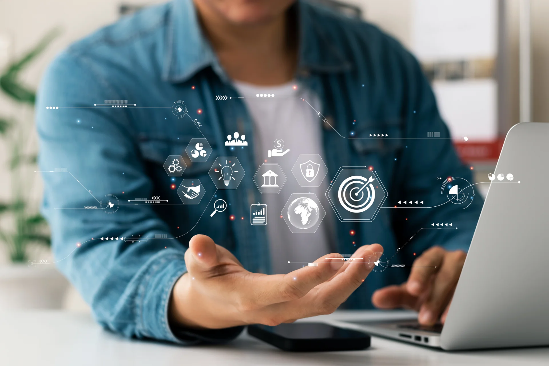 Person mit ausgestreckter Hand vor einem Laptop mit schwebenden digitalen Icons für Geschäftsprozesse wie Zielscheibe, Handschlag, und Sicherheit.