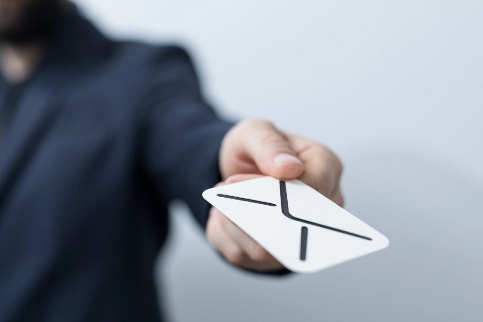 Person hält eine weiße Karte mit einem schwarzen Briefumschlag-Symbol nach vorne.
