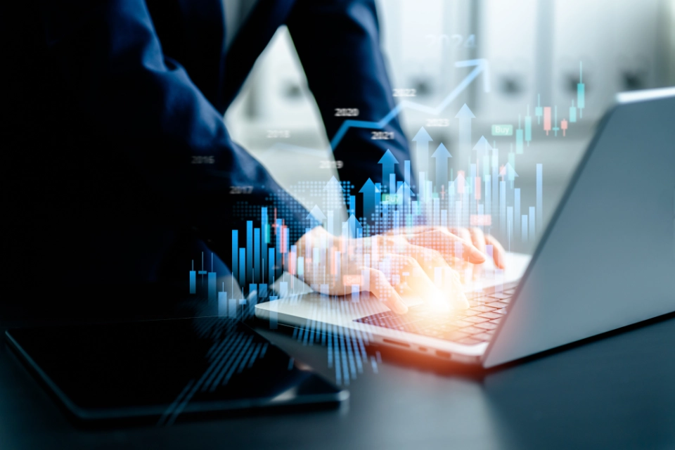 Person tippt auf einem Laptop mit überlagerten Grafikdiagrammen und Aufwärtstrends.