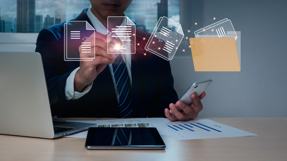 Geschäftsmann am Schreibtisch mit Laptop, Tablet und Smartphone, der digitale Dokumente in einem Ordner verwaltet.