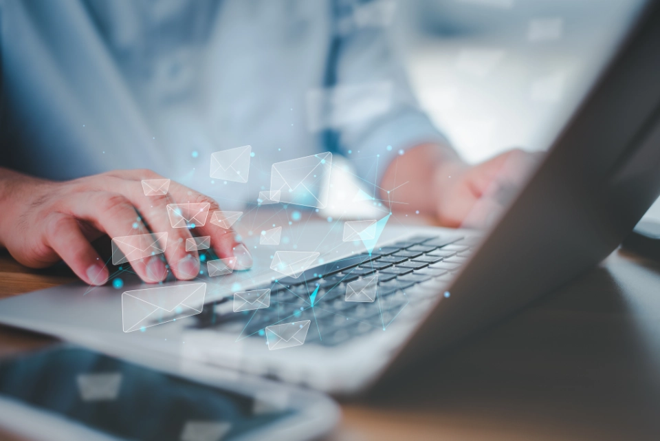 Person tippt auf Laptop-Tastatur, umgeben von digitalen E-Mail-Symbolen.