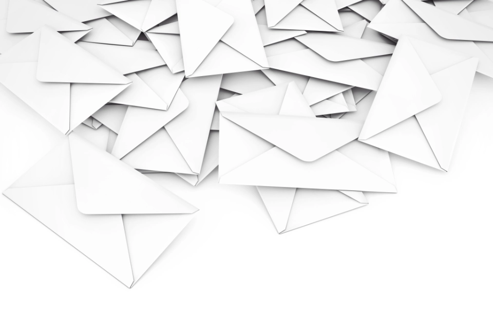 Viele weiße, verschlossene Briefumschläge sind ungeordnet auf einer weißen Oberfläche verteilt.