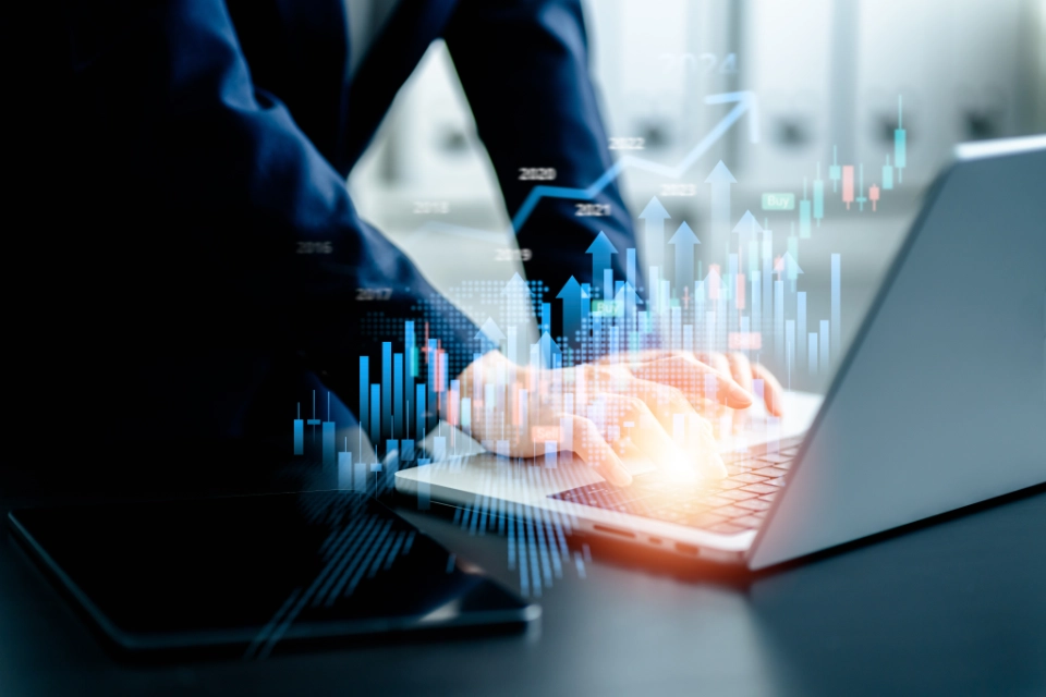 Person in business attire typing on a laptop with digital financial charts and upward arrows overlaid, indicating data analysis or market growth.