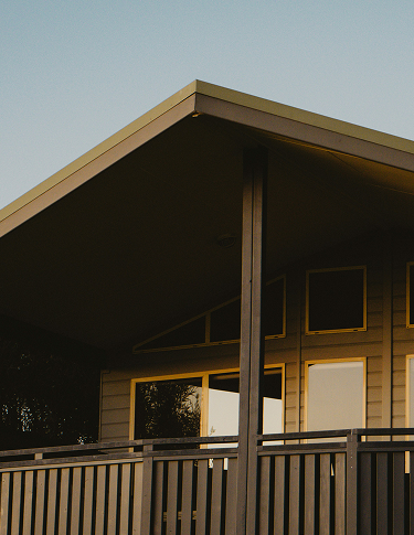 Modern house with a sharply angled roof and large windows reflecting trees at dusk.