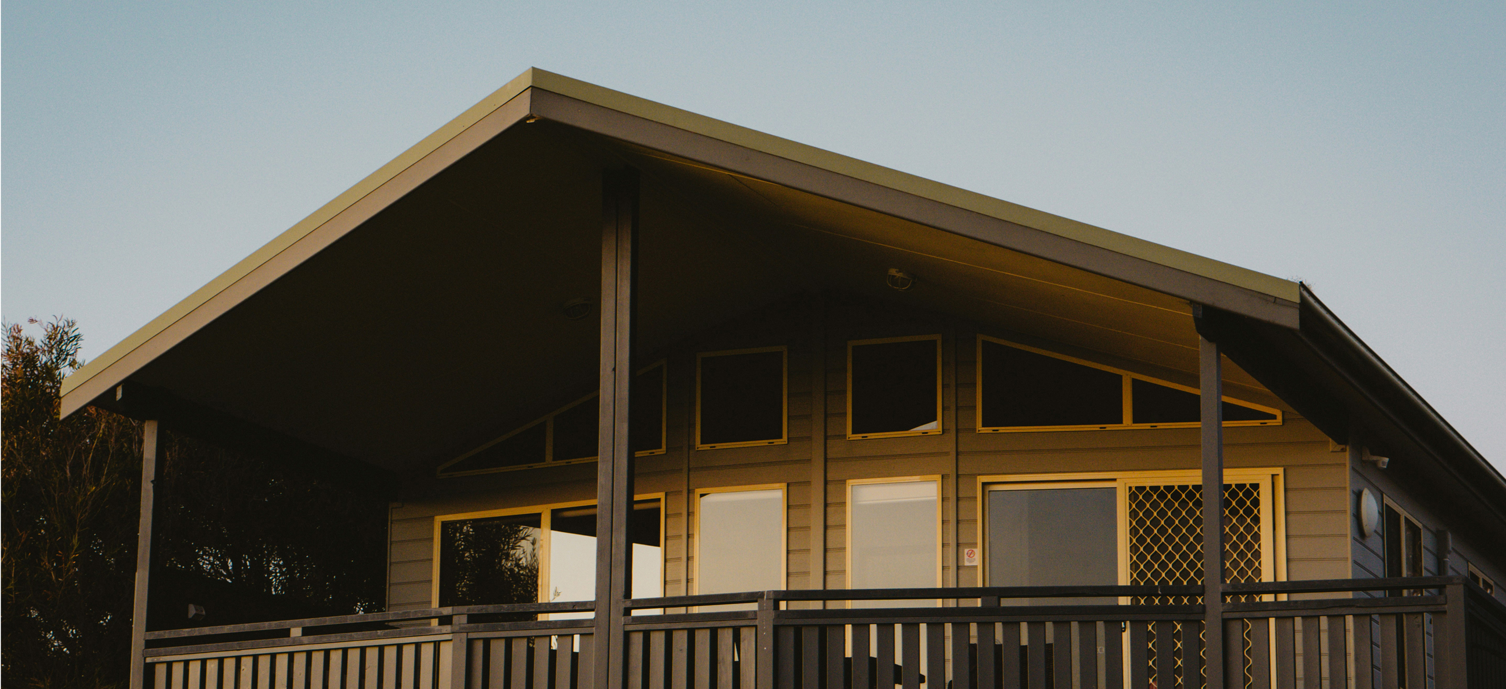 Modern house with beige siding, large windows, and a covered porch with railing at sunset.