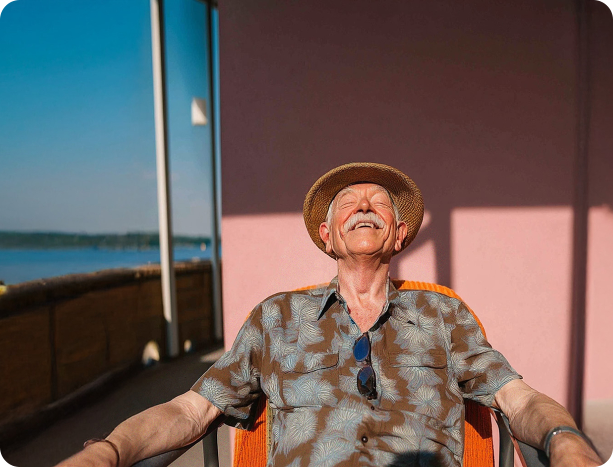 Elderly man with a mustache and straw hat sitting outdoors, smiling with eyes closed, enjoying the sun.
