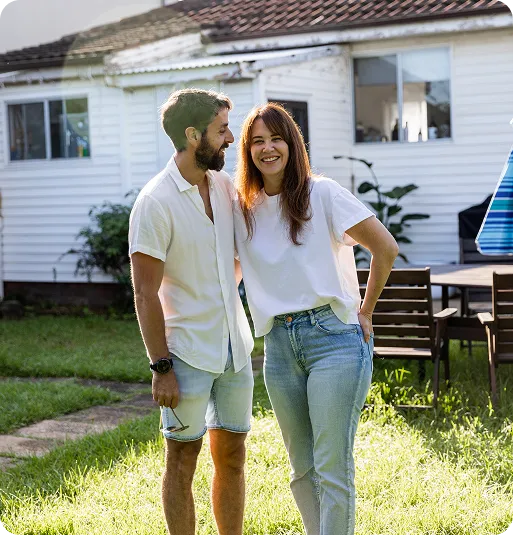 A man and woman smiling and standing together outside in a sunny backyard.