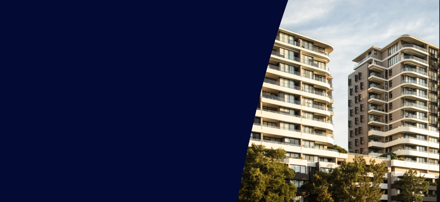 Modern residential buildings with balconies and trees below under a cloudy sky.