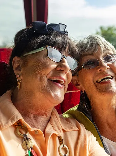 Two elderly women smiling and enjoying a moment together indoors near a window.