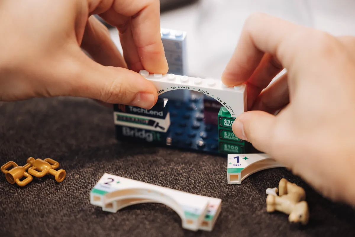 Hands assembling a small model from Bridgit-branded building blocks.