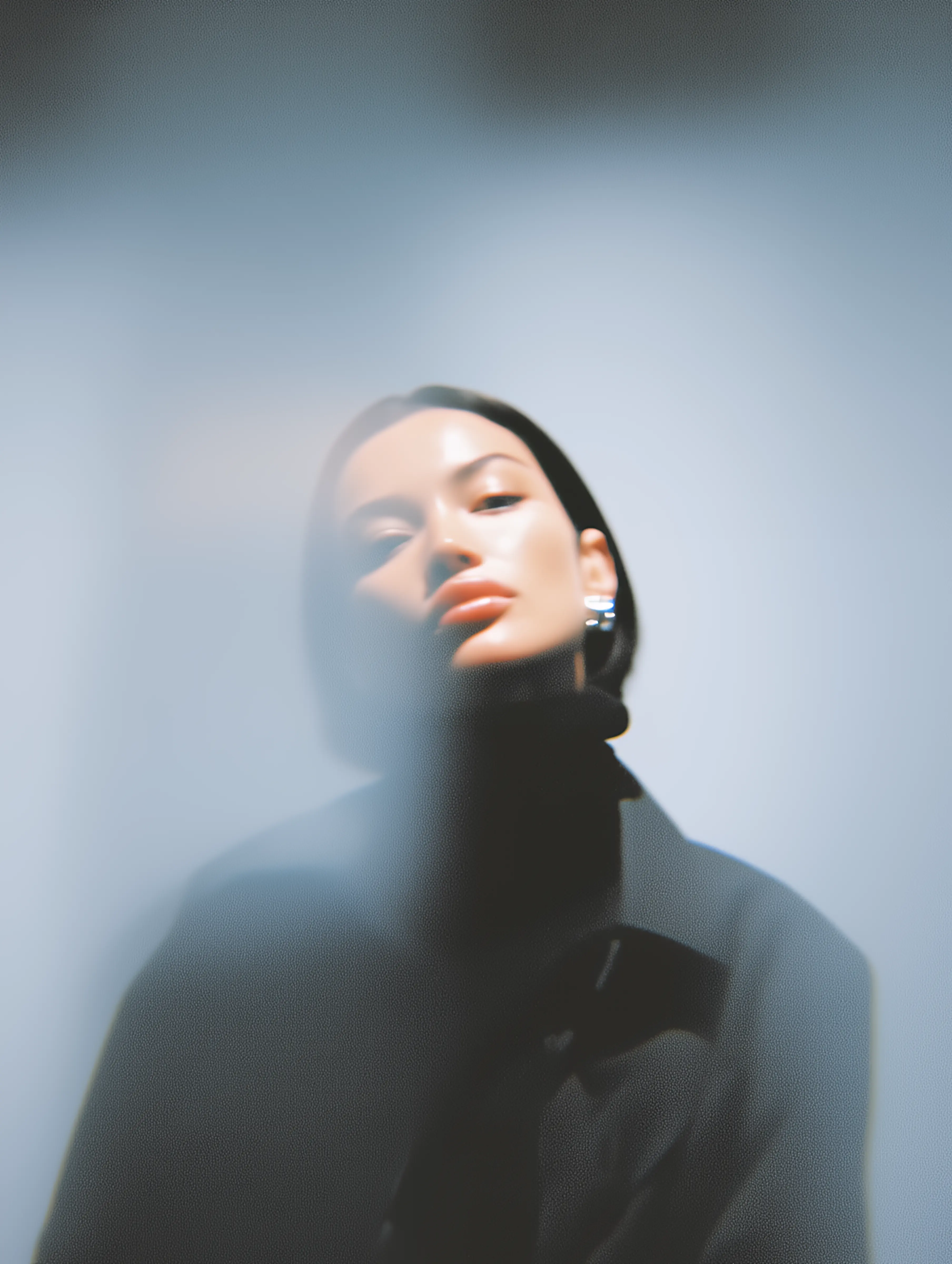 Stylish portrait of a woman with dark hair wearing silver earrings and a black turtleneck, blurred with soft lighting.