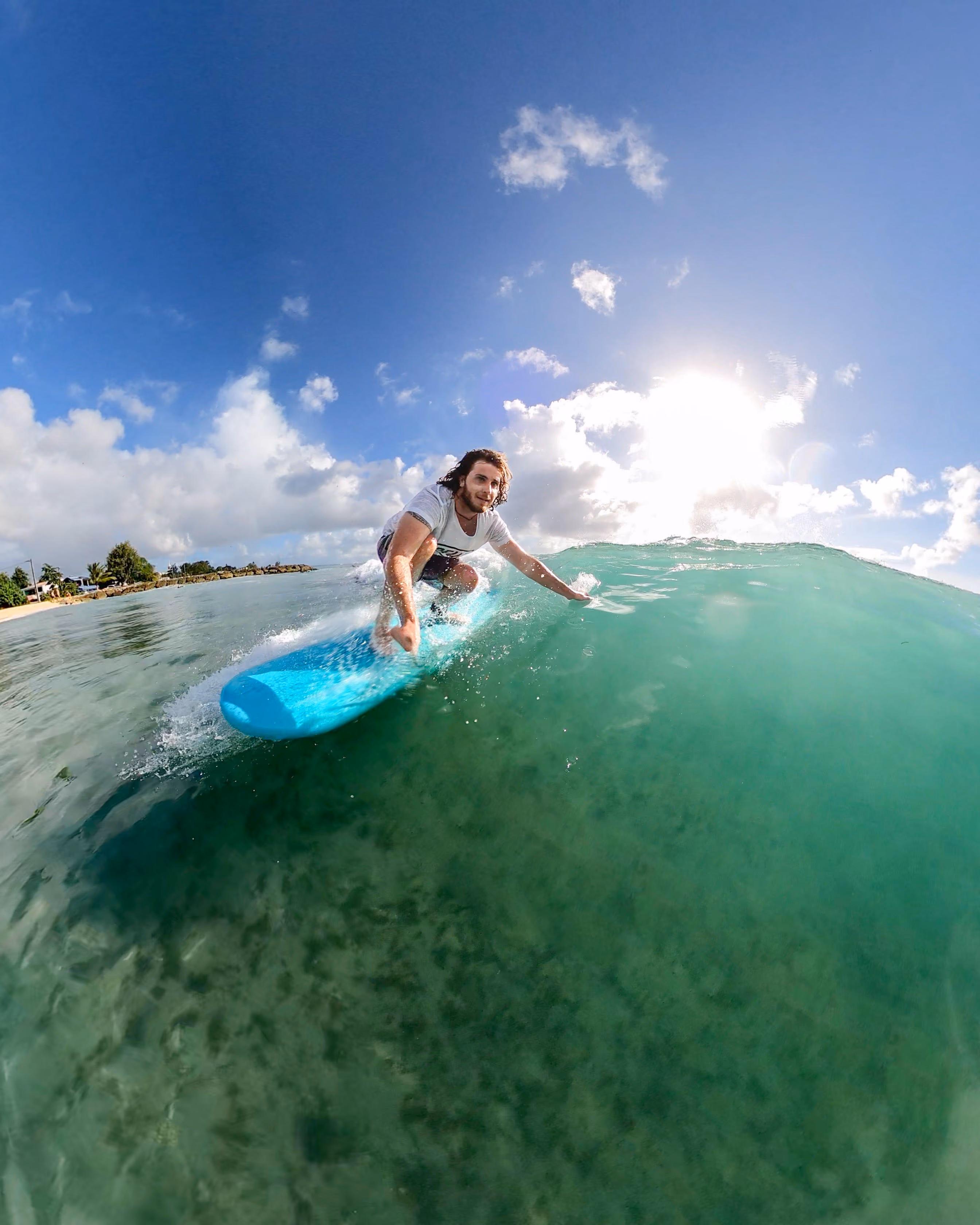 Un homme surfant une grande vague sur une planche bleue sous un ciel ensoleillé.