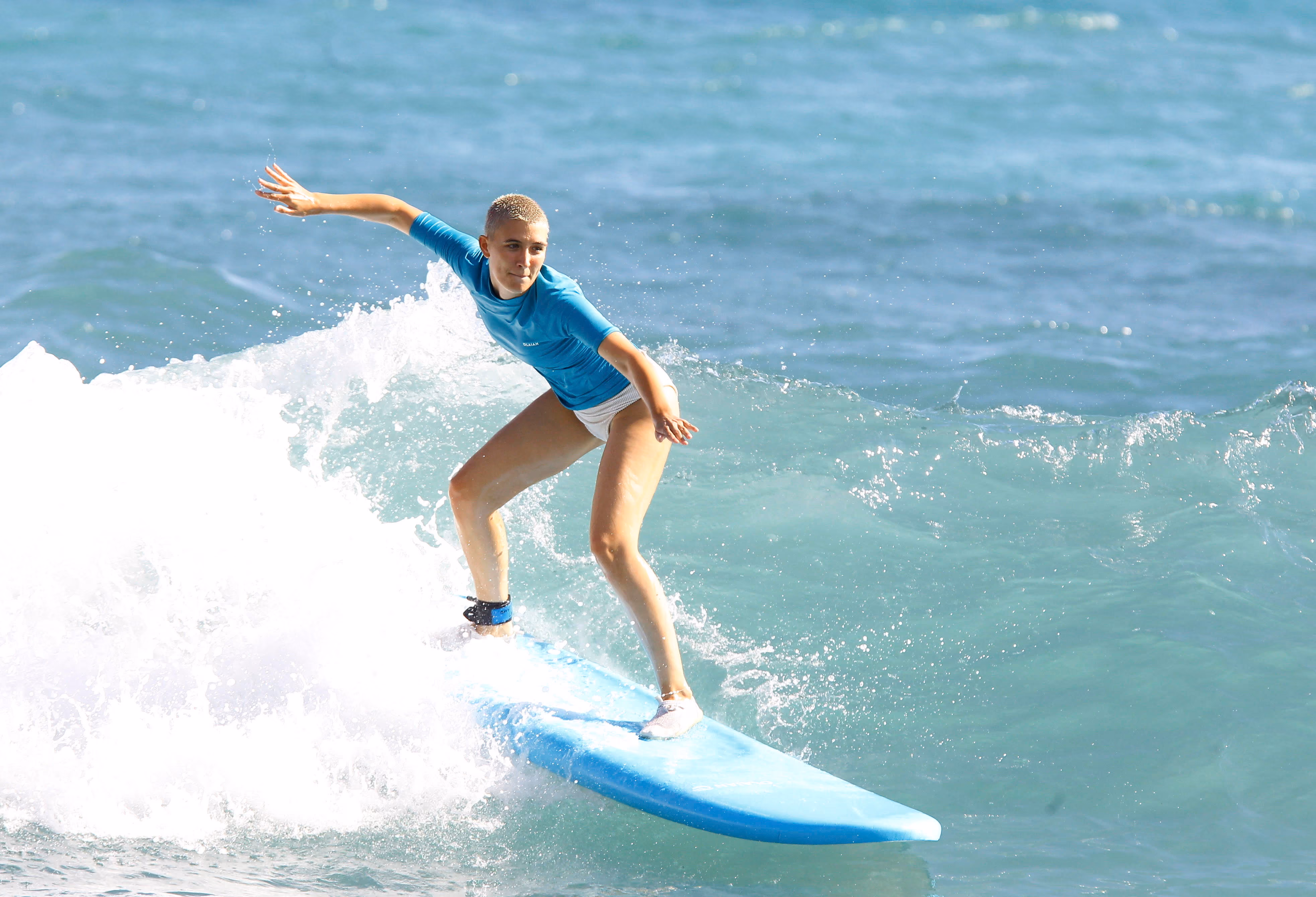 Jeune femme en haut bleu surfant sur une planche bleue sur une vague en mer.