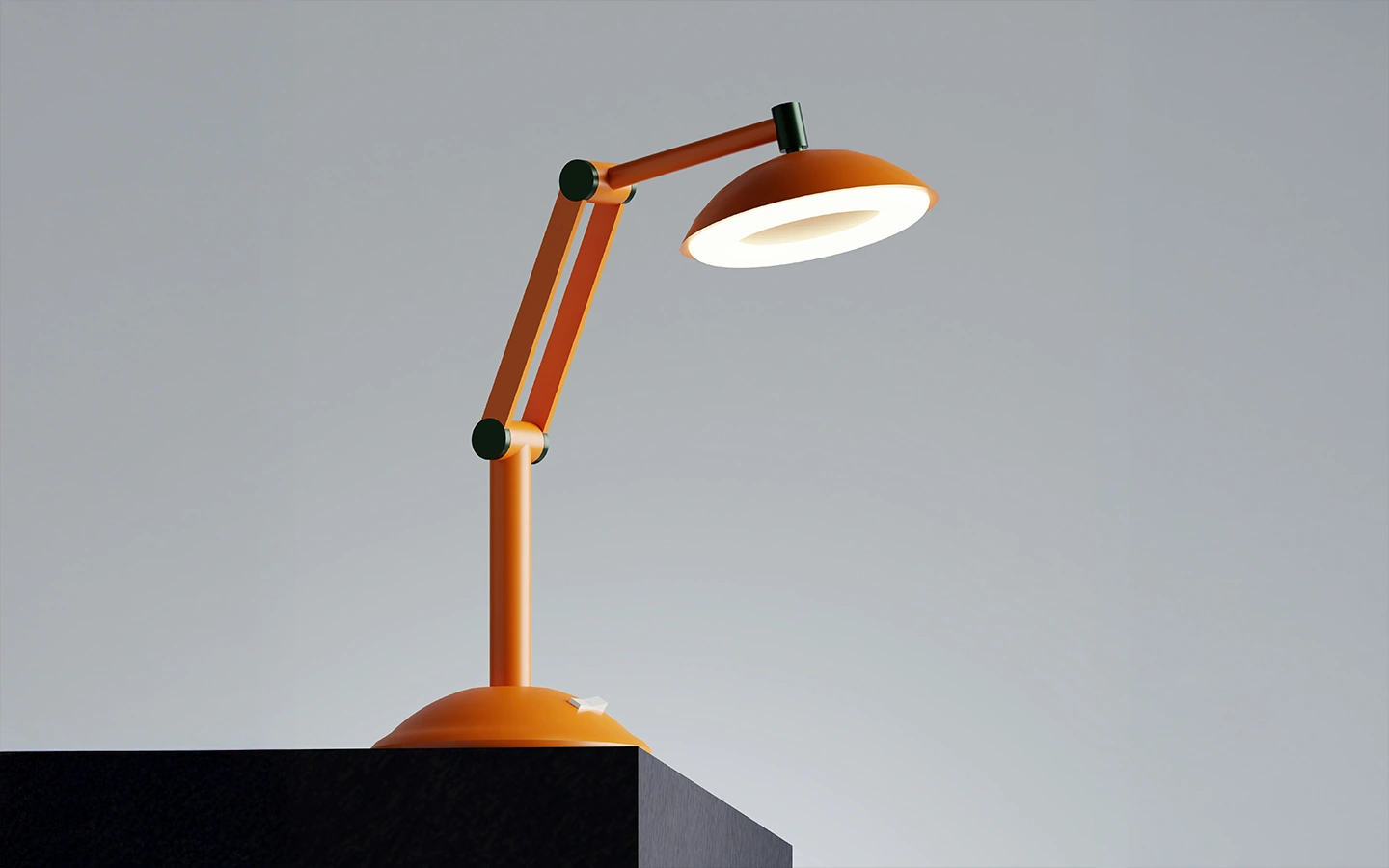 Orange adjustable desk lamp lit on the edge of a black surface with a plain gray background.