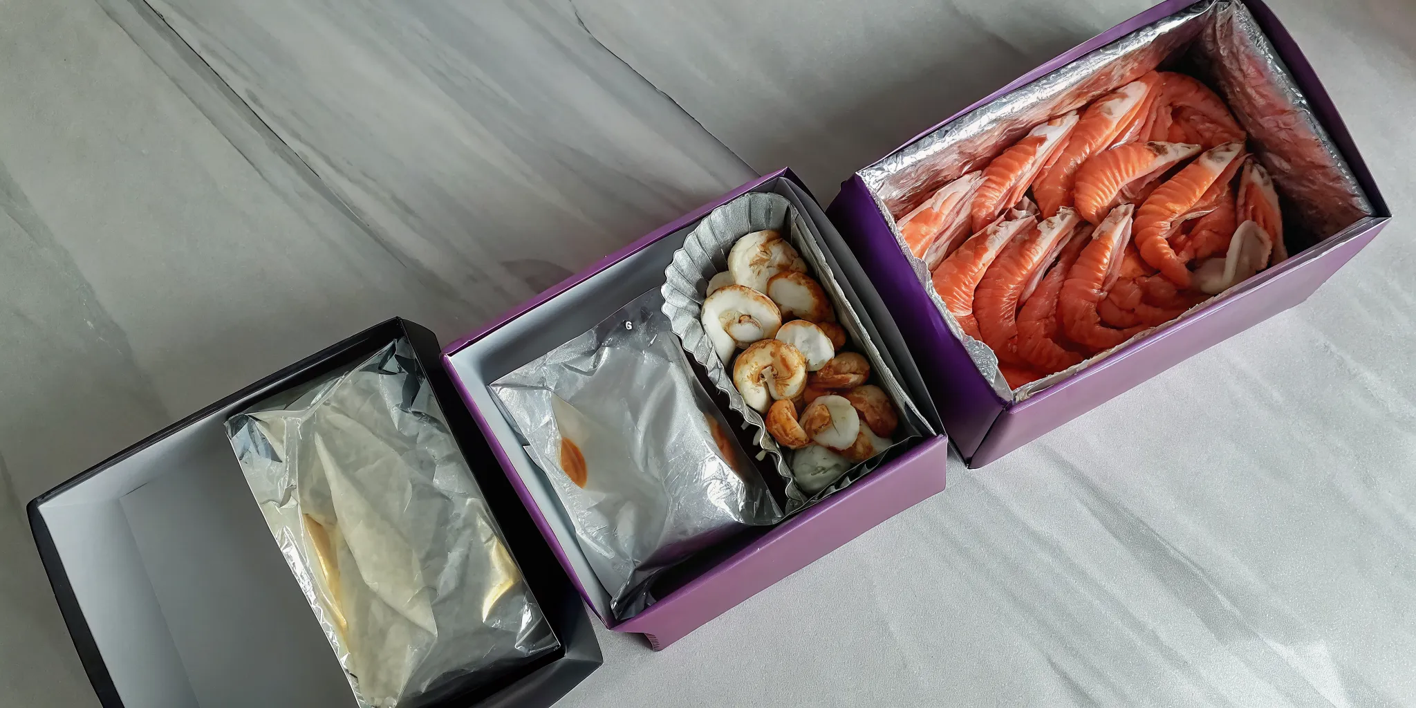 A seafood delivery box with portions of salmon, shrimp, and scallops packed on ice.