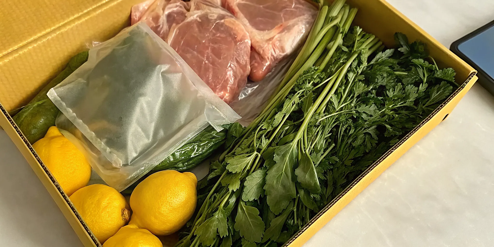 A safe online meat order delivered in a box with vacuum-sealed cuts, herbs, and lemons.