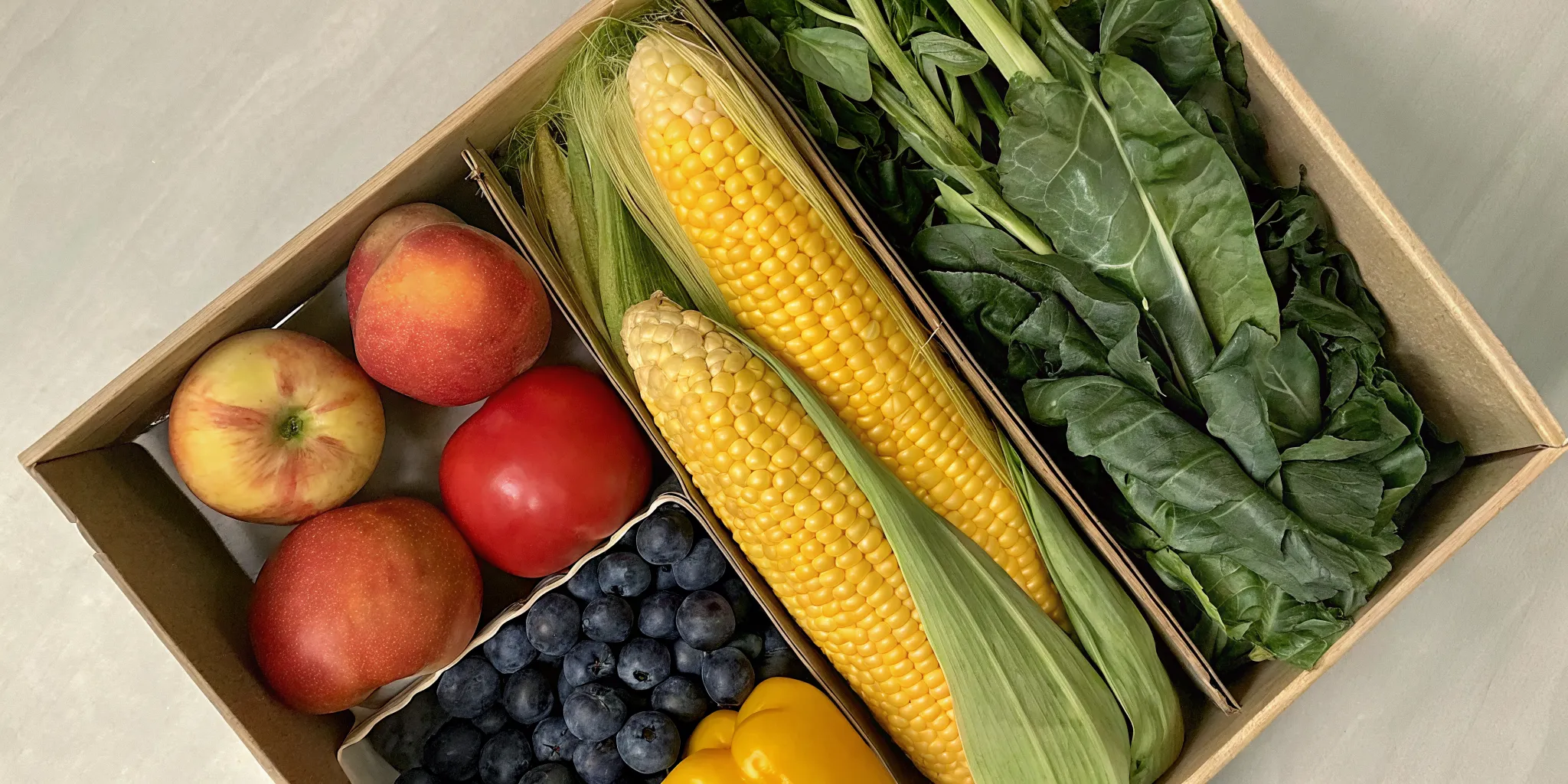 A local Ontario food subscription box filled with fresh corn, leafy greens, apples, and other produce.