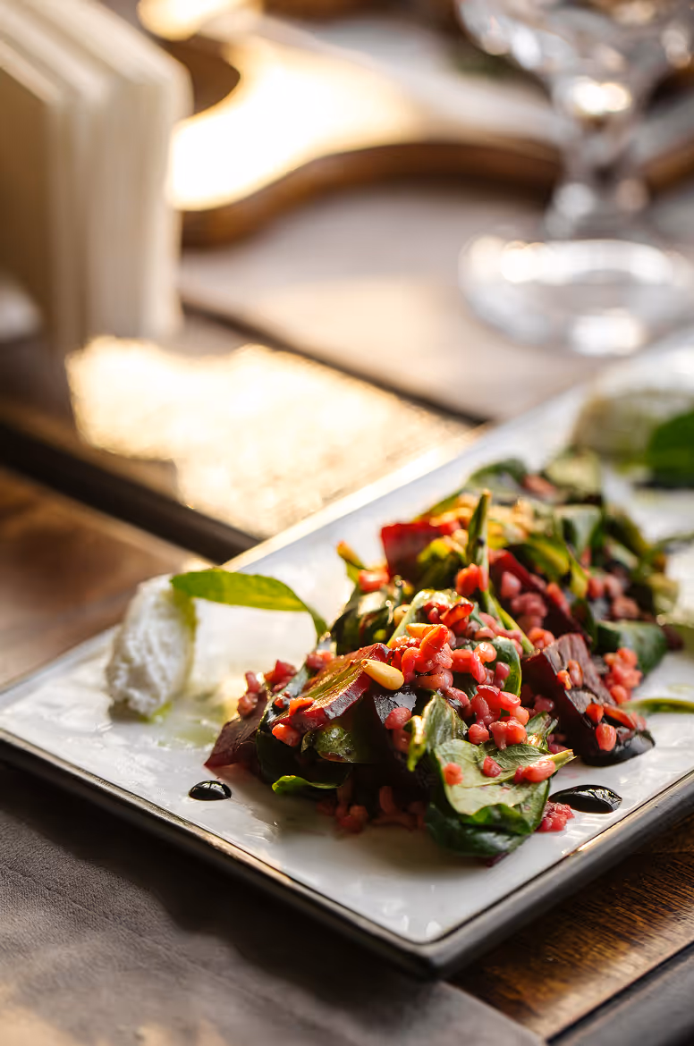 Plate of fresh salad with spinach, roasted beets, pine nuts, pomegranate seeds, and dollops of creamy cheese.