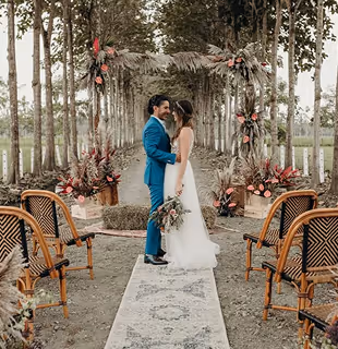 Wedding couple under a floral arch in a tree-lined driveway at Hacienda La Danesa.