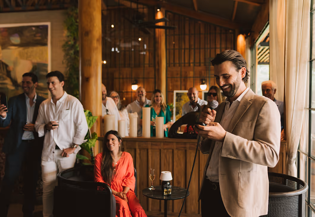 Man in beige suit giving a speech with a microphone at an indoor reception, Hacienda La Danesa.