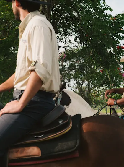 A medium shot of a man on horseback, showing his light beige shirt and western saddle.