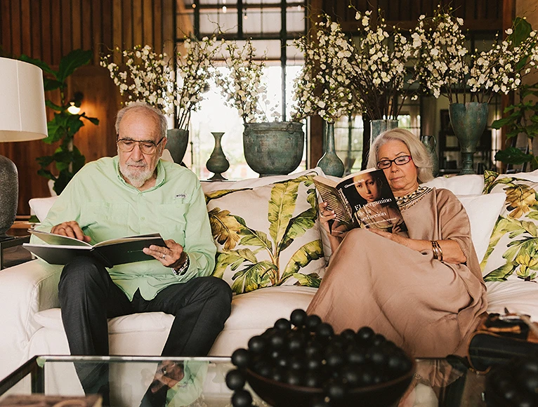Couple reading books on a white sofa surrounded by flowers in the lounge of Hacienda La Danesa