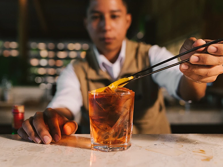 Bartender garnishing an Old Fashioned cocktail with orange peel at Hacienda La Danesa bar