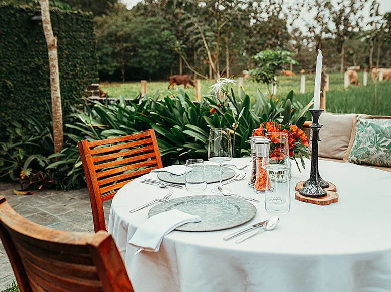 Outdoor dining table set for two at Hacienda La Danesa with candle, tropical flowers and grazing cattle in the background