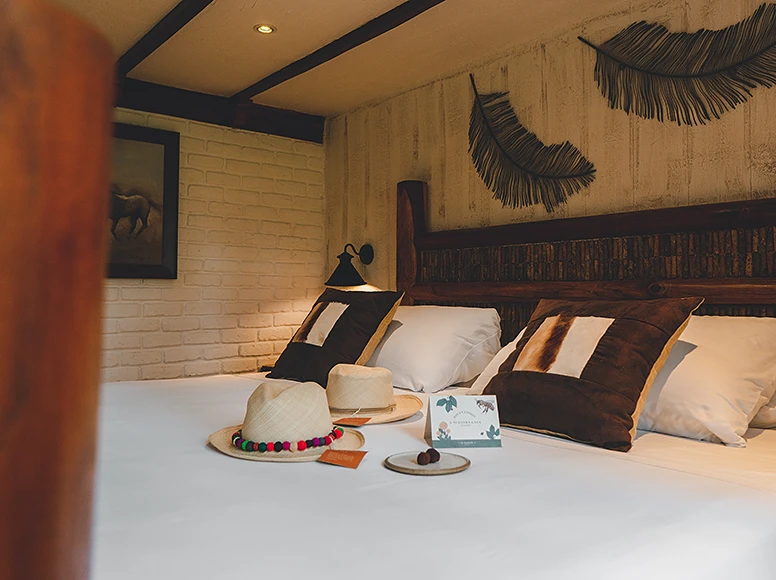 Heritage bedroom at Hacienda La Danesa with rustic wood headboard, palm leaf wall art and welcome chocolate