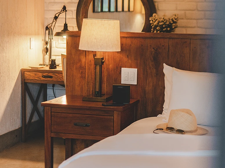 Rustic wooden bedside table with lamp, Bose speaker and panama hat on bed at Hacienda La Danesa