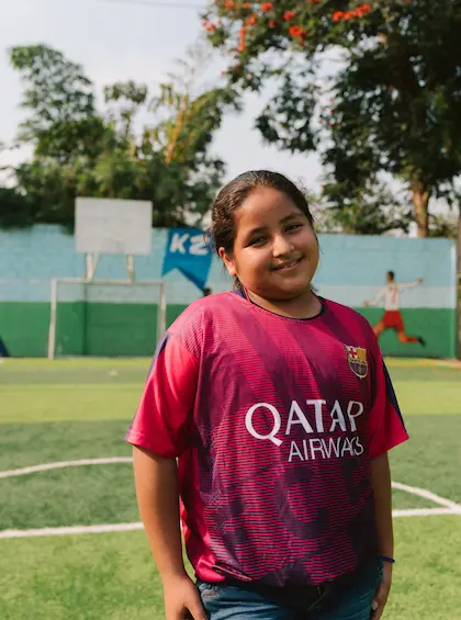 Smiling young girl from the local community on a football pitch supported by Hacienda La Danesa in Naranjito