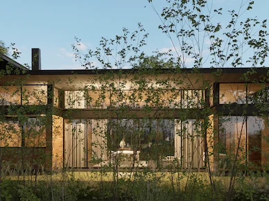 Evening facade of Hacienda La Danesa private residence with climbing vines on the two-story structure and warm light glowing through large picture windows