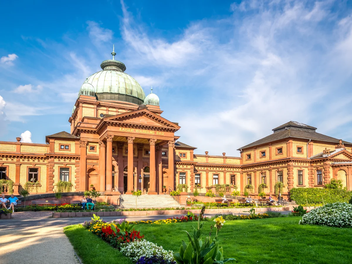 Historisches Gebäude Kaiser Wilhelms Bad mit Kuppel und Garten unter blauem Himmel in Bad Homburg.