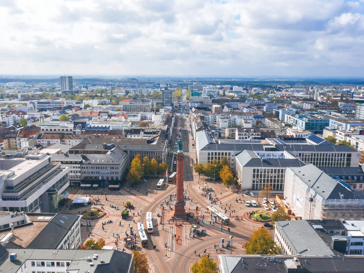 Luftaufnahme eines Platzes mit Säule und Statue inmitten einer Stadt mit Gebäuden und Straßen.