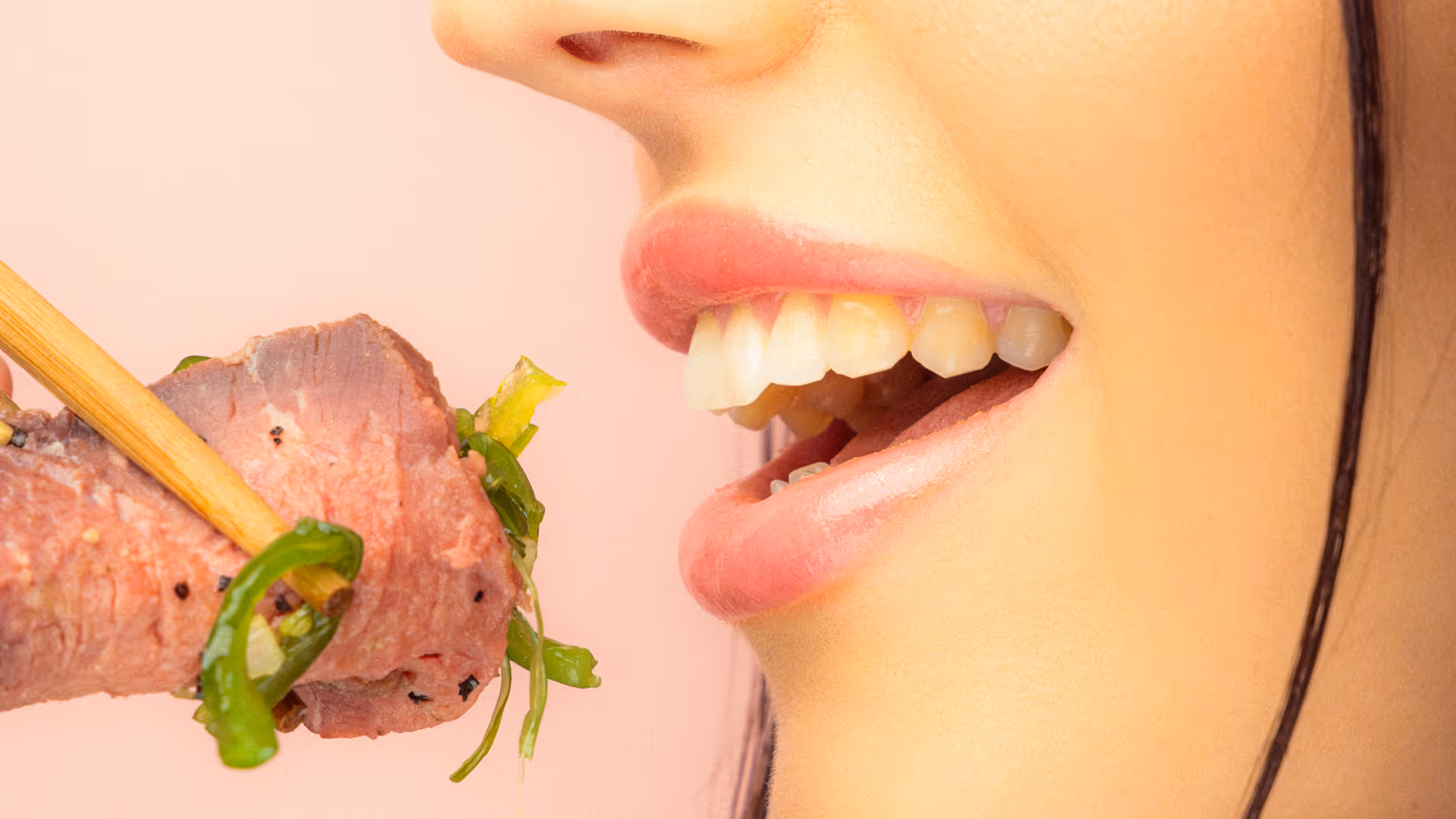 Nahaufnahme einer Person, die mit Stäbchen ein Stück Fleisch und grünes Gemüse zum Mund führt.