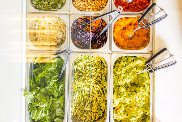 Salatbar mit verschiedenen frischen Zutaten wie Spinat, geraspeltem Käse, Kichererbsen, gehacktem Gemüse, Kürbispüree und Avocadocreme.