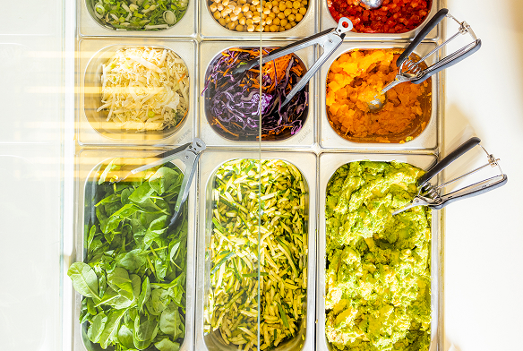 Salatbar mit verschiedenen frischen Zutaten wie Spinat, geraspeltem Käse, Kichererbsen, gehacktem Gemüse, Kürbispüree und Avocadocreme.